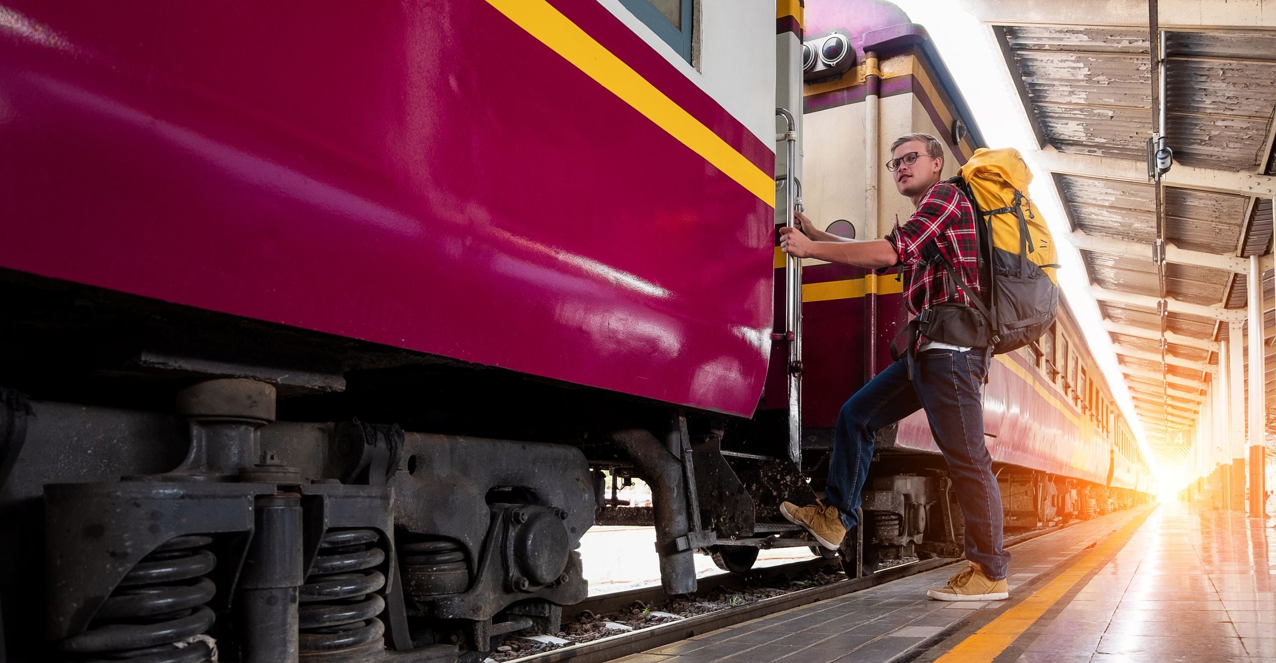 Man with backpack boarding a train at urban railway station during daytime travel adventure.